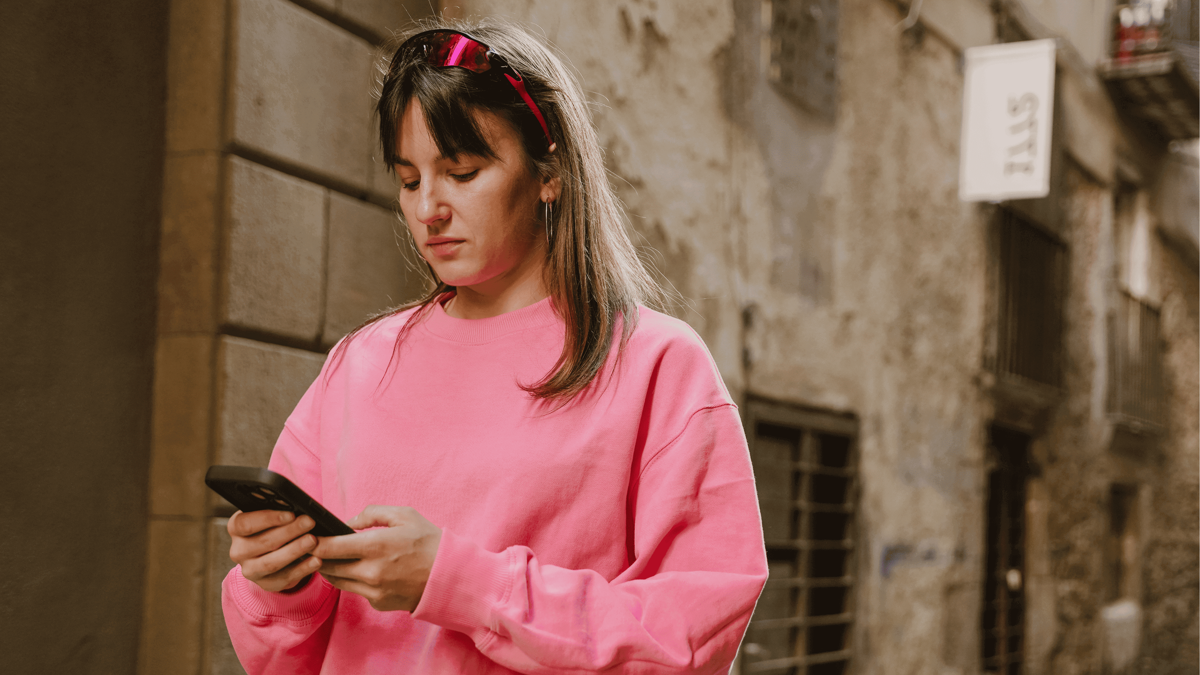 Woman in pink jumper using her phone in a city street