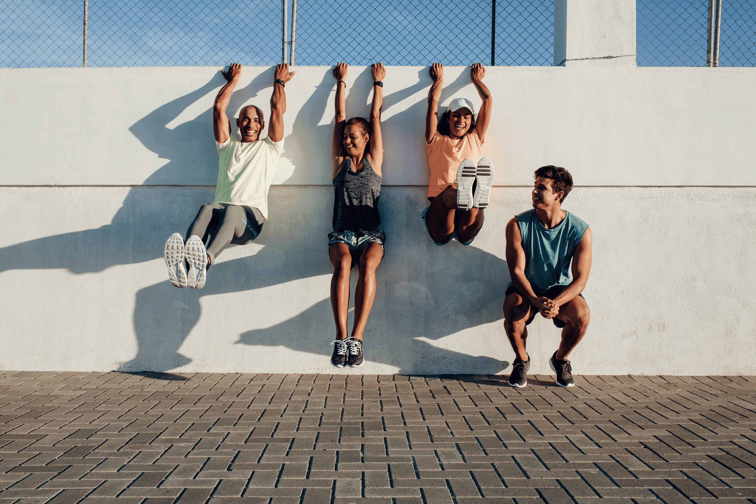 Friends laughing as they hang from a sunny wall